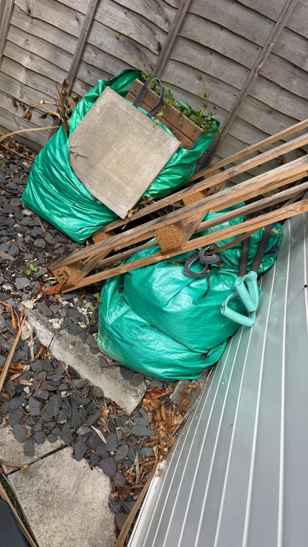 Green garden waste bags and timber beside a fence awaiting collection in Wimborne, Dorset