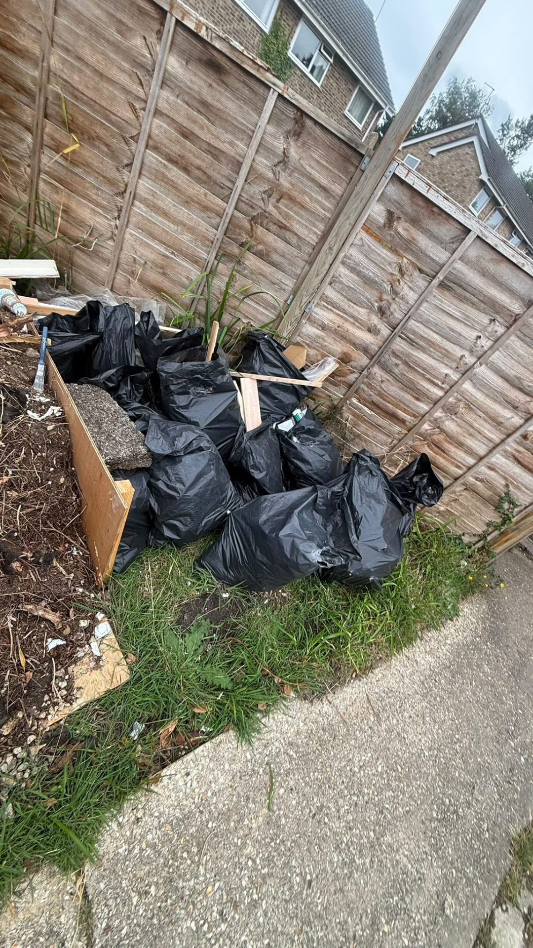 Black bags and garden rubbish along a fence awaiting collection in Wimborne, Dorset