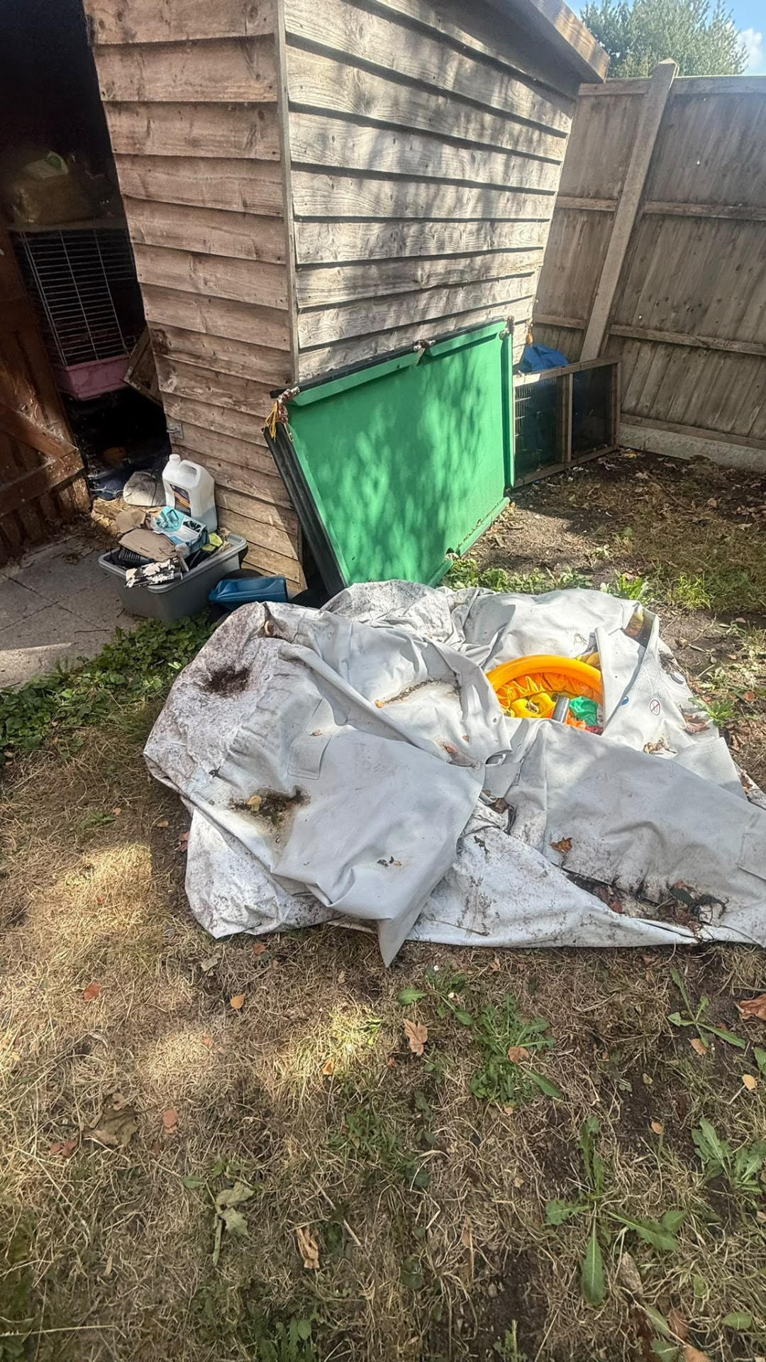 Garden clutter, bags and tarp beside a wooden shed before clearance in Wimborne, Dorset