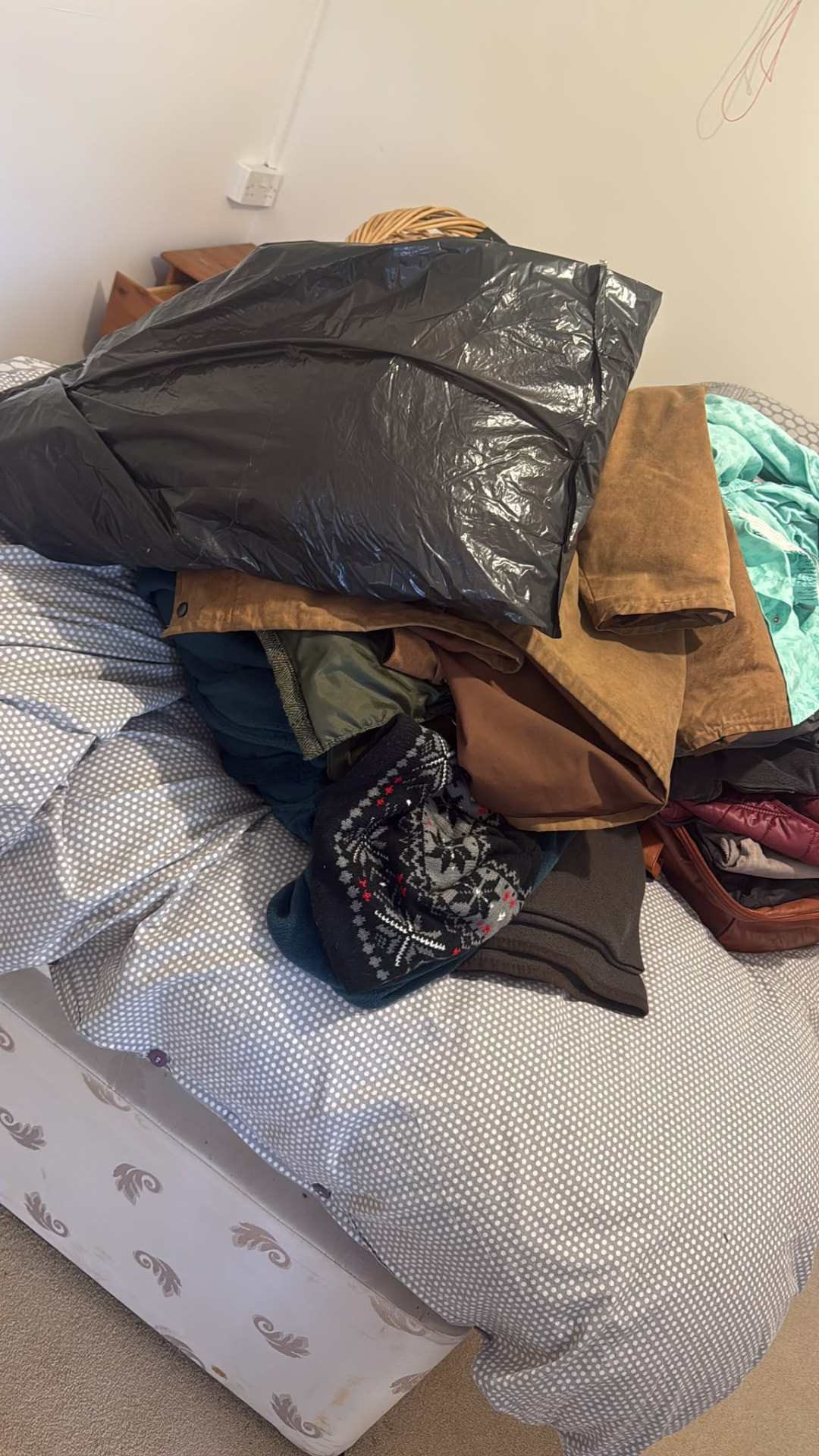 Bed covered in clothing and bags before a house clearance in Wimborne, Dorset
